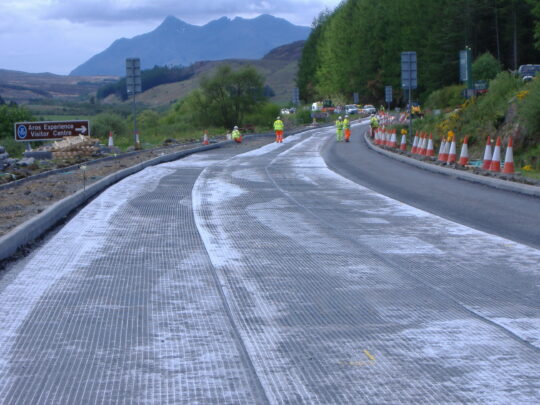 Rotaflex laid to the edge of the road surface to minimise edge failure over the peaty soils beneath. Rotaflex has been bonded to the surface, ready to receive the final surface coarse layer. The bitumen saturates the Rotaflex, embedding it as a stiff waterproof layer between the road surface layers to prevent cracks and water infiltration.